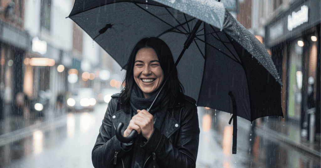 A woman beams with laughter while holding an open umbrella during a heavy rain downpour, visually demonstrating the joyful resilience found when you learn how to stop handing over emotional access too soon.