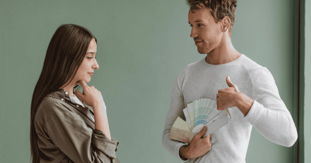 A man gestures confidently while showing a color swatch fan to a thoughtful woman, depicting how easily manipulative narratives can be disguised as helpful guidance.