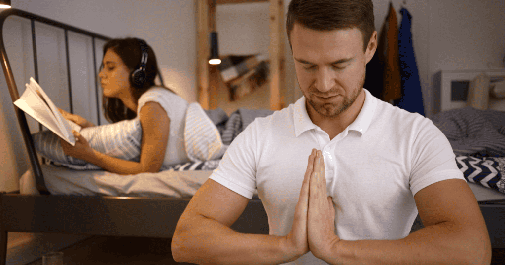 A man performing a sudden display of meditation and prayer beside his disengaged partner, depicting how a narcissist briefly adopts spirituality or emotional depth as a tactical reset to make you forget what they just did.