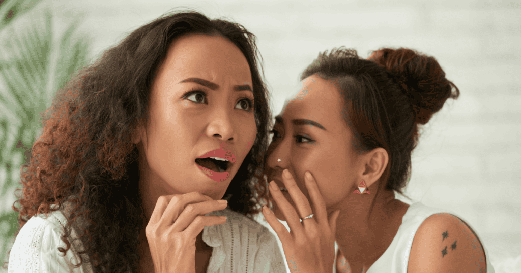 A woman whispering into another's ear as she reacts with wide-eyed shock, illustrating how a narcissist spreads damaging lies behind your back to turn others against you before you even realize it.