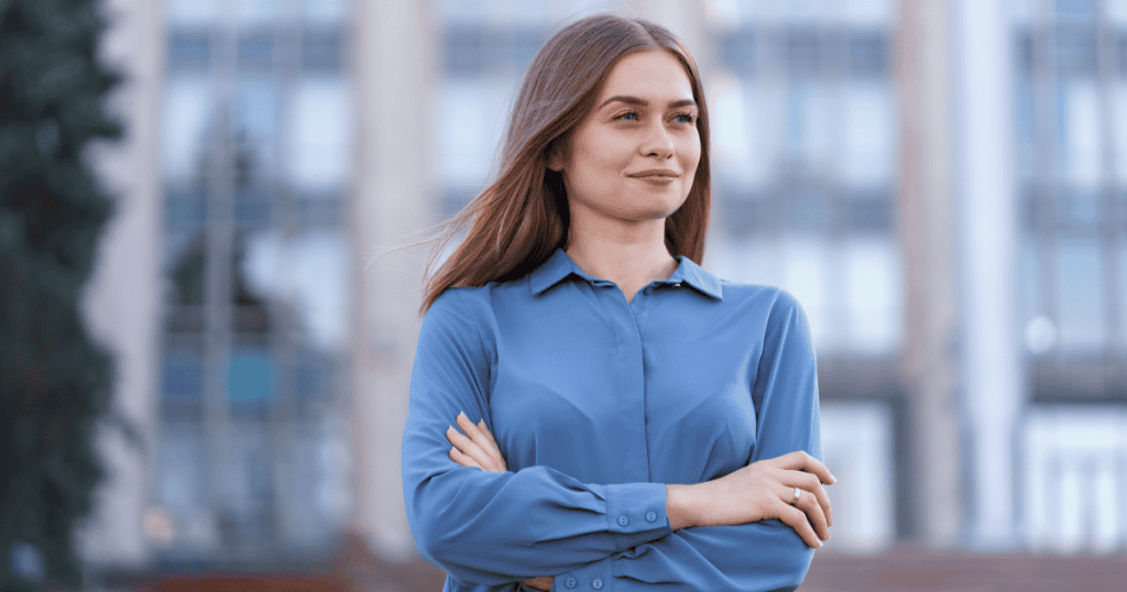 A woman standing with arms crossed and a composed, knowing smile, representing the awareness and quiet strength a woman gains once she recognizes the pattern behind a narcissistic man's contempt.