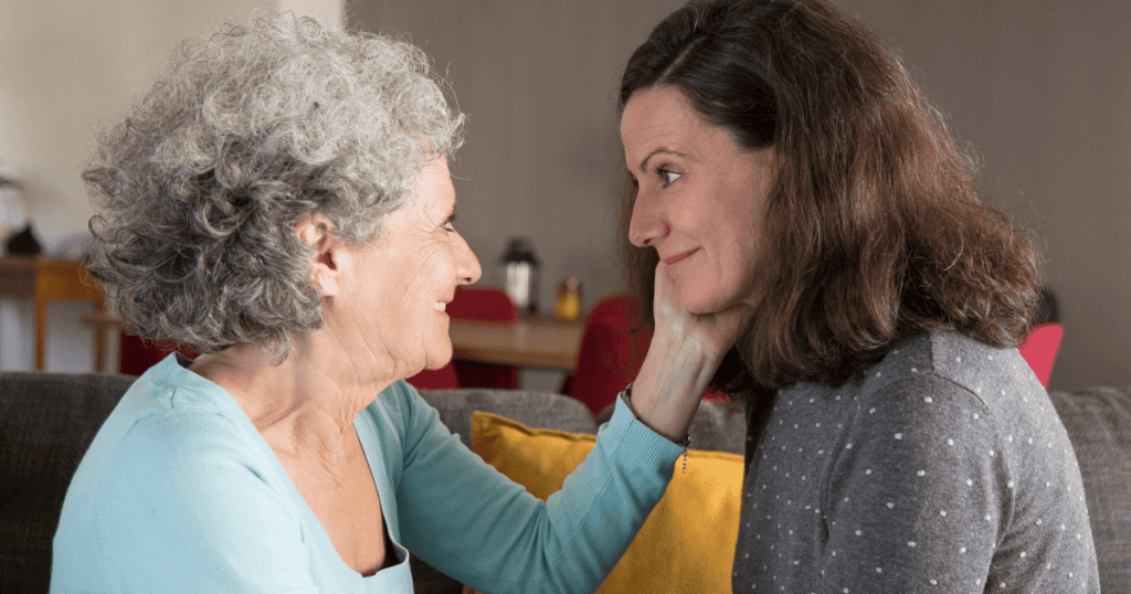 An older woman cups a younger woman's chin while smiling tenderly, capturing how sudden affectionate gestures are used to sweep historical hurts under the rug.