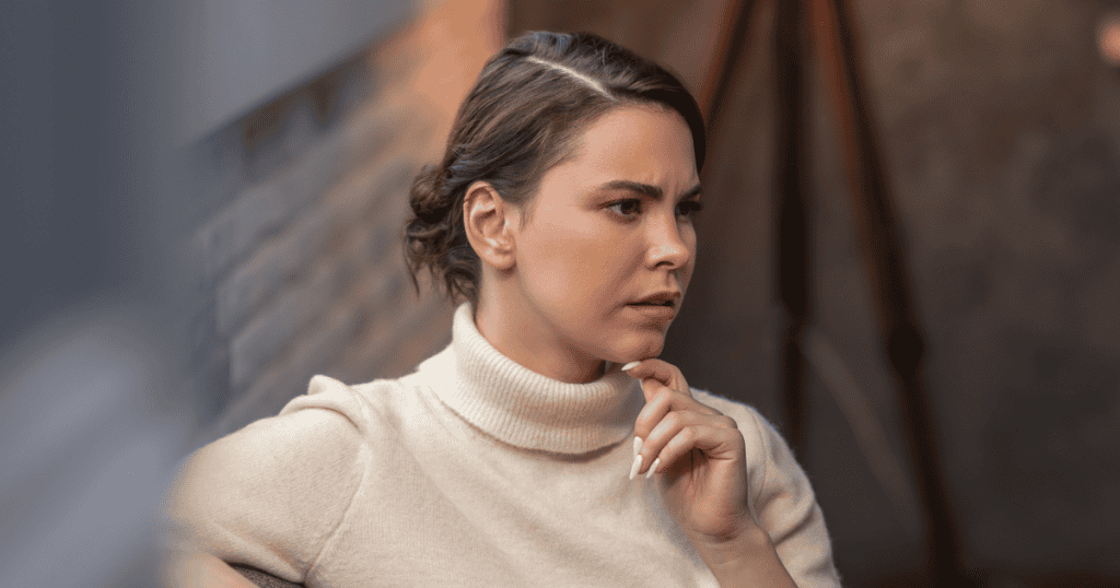 A woman with her hair in a neat bun rests her chin thoughtfully on her hand with a furrowed brow, reflecting the quiet focus needed to carefully analyze complex interpersonal dynamics.