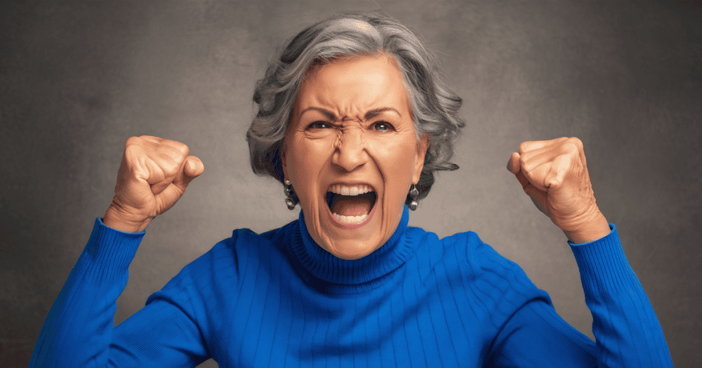 A gray-haired woman clenches her raised fists and screams in furious outrage, showcasing the explosive hostility that erupts when long-held control begins to slip away.