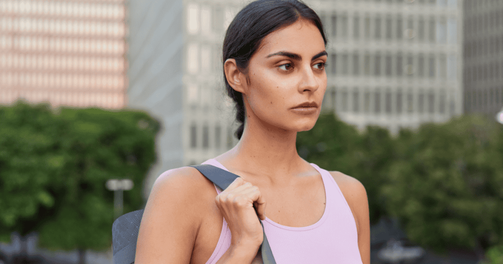 A composed, city-dressed woman glances off to the side with a guarded expression, embodying the quiet strength that can be turned against her.