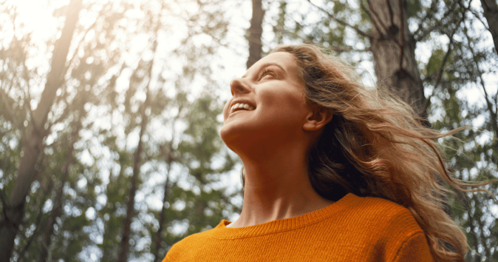A woman smiling freely beneath sunlit trees, reminding you that recognizing the signs of a narcissistic upbringing isn't the end of your story ā it's where healing begins.