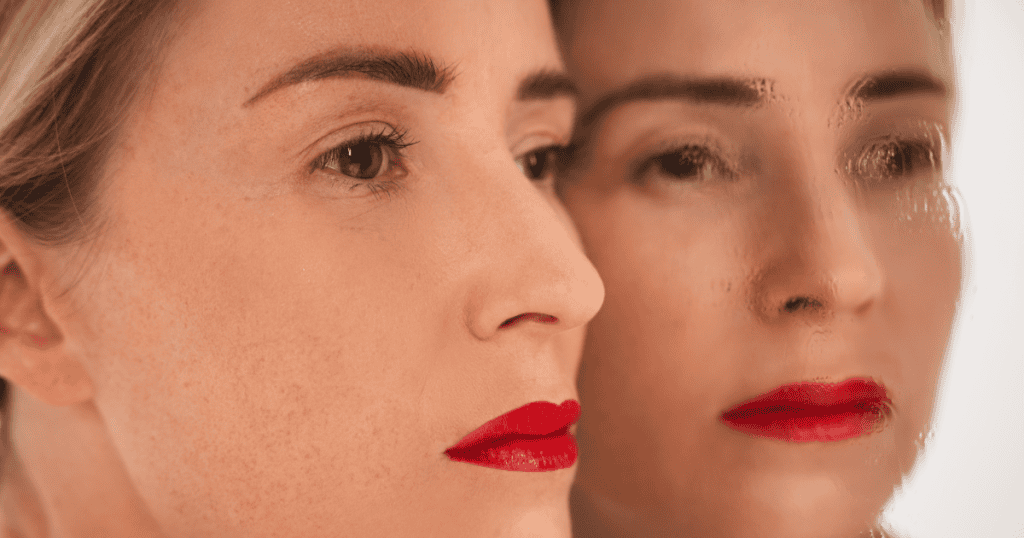 A close-up double exposure shows a woman's face mirrored in sharp focus and soft blur, symbolizing the gap between a confident public front and the person hidden behind closed doors.