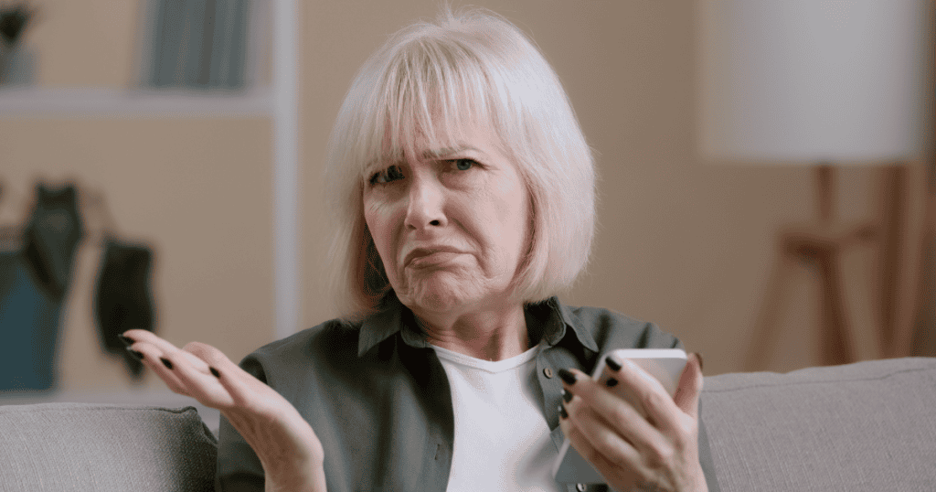 A woman shrugs with a confused, exasperated frown while holding her phone, capturing the puzzling contradiction at the heart of emotional avoidance.