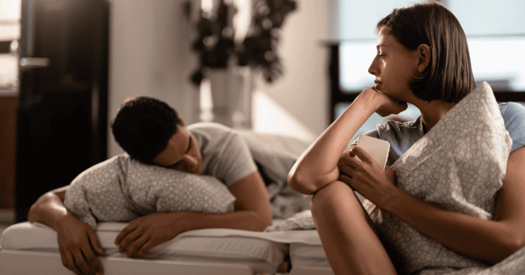 A woman sitting awake in bed clutching a pillow, staring into the distance while her partner sleeps, capturing the devastating clarity of the moment she realizes the marriage was never about love.