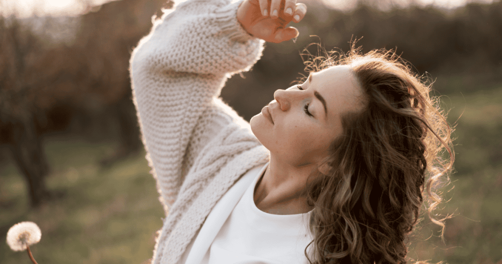 A woman raises her arm and tilts her face toward the sunlight with eyes closed, embodying the freedom of releasing a burden that was never hers to carry.