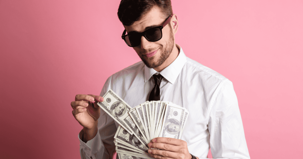 A smug man in sunglasses and a tie fans out a thick stack of hundred-dollar bills, capturing the self-satisfied entitlement a narcissist often shows when money is within reach.