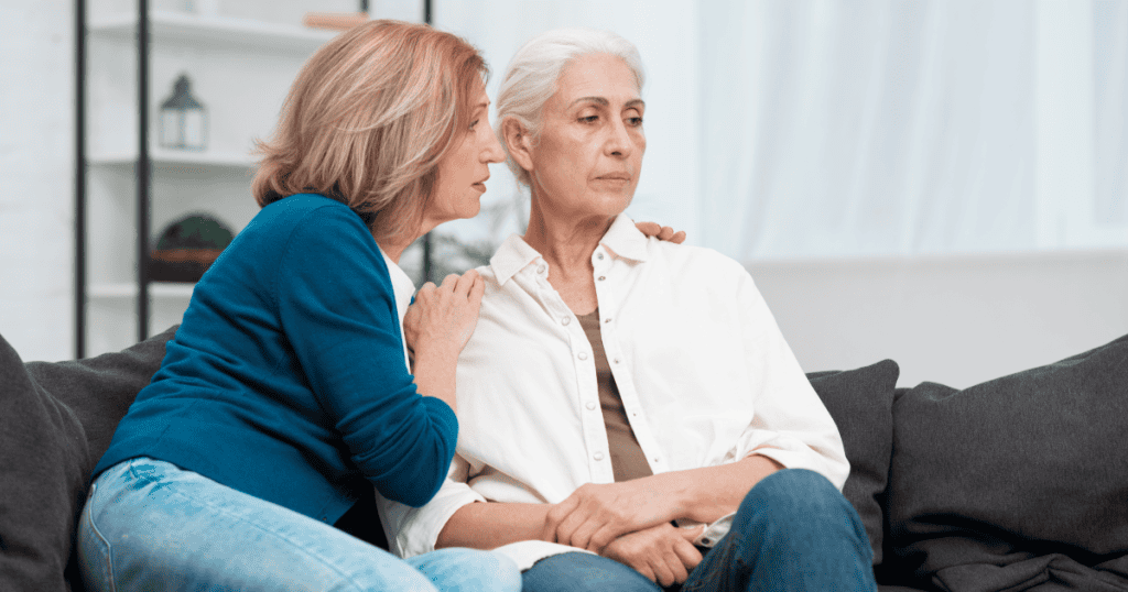 One woman gently touches another's shoulder in comfort while she stares distantly ahead, unmoved and withdrawn, illustrating what intimacy avoidance can look like away from public view.
