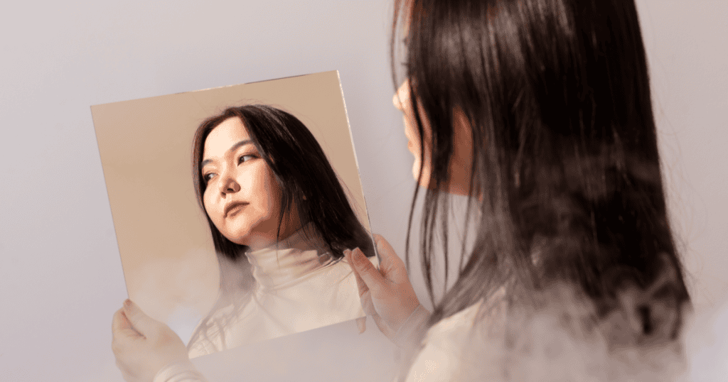 A woman staring blankly at her own reflection, capturing the identity confusion of someone raised by a narcissist who never allowed them to develop a true sense of self.