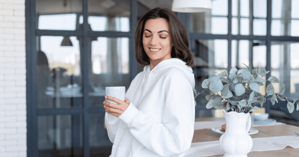 A woman smiles softly while holding a warm mug in a sunlit kitchen, embodying the quiet confidence of trusting her own feelings without needing proof.