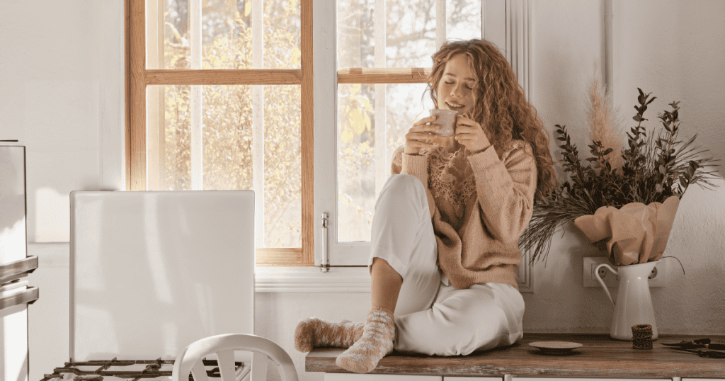A woman sitting peacefully in a sunlit kitchen cradling a warm mug, embodying the calm that comes from finally trusting that everything her body felt during the abuse was real and valid.