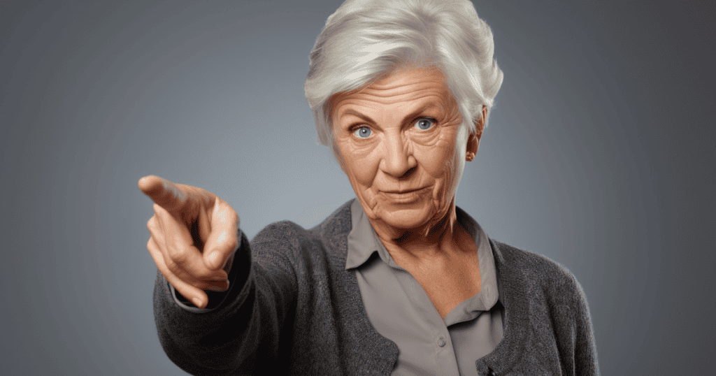 An older woman points a stern, accusing finger directly forward with a sharp gaze, illustrating the rigid labeling and scapegoating imposed to deflect accountability.