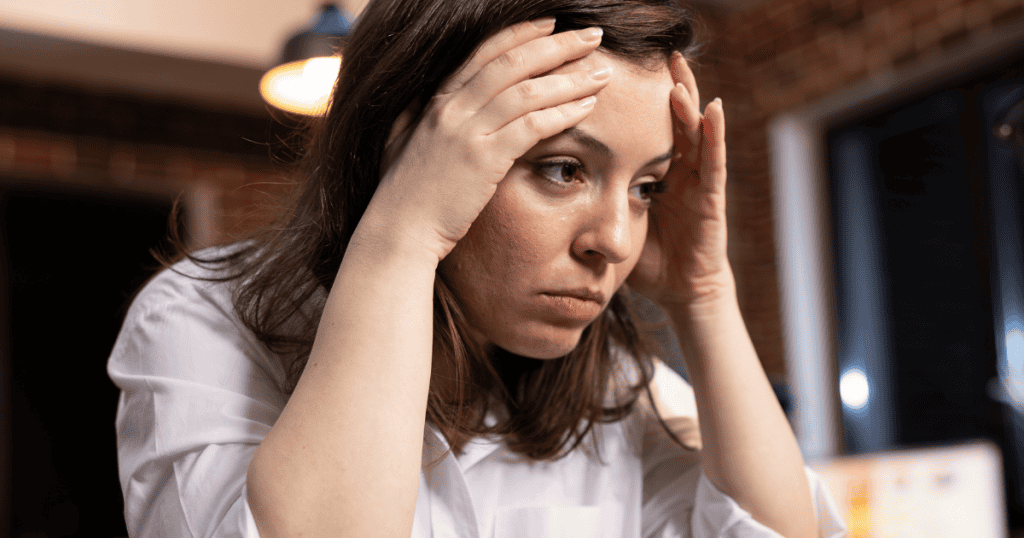A woman clutches the sides of her forehead with an expression of weary desolation, capturing the profound mental exhaustion that comes from enduring relentless mistreatment.