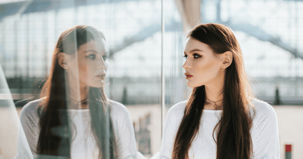 A woman stands composed and steady as she looks at her reflection against a glass panel, illustrating the profound self-validation needed to reclaim your worth.