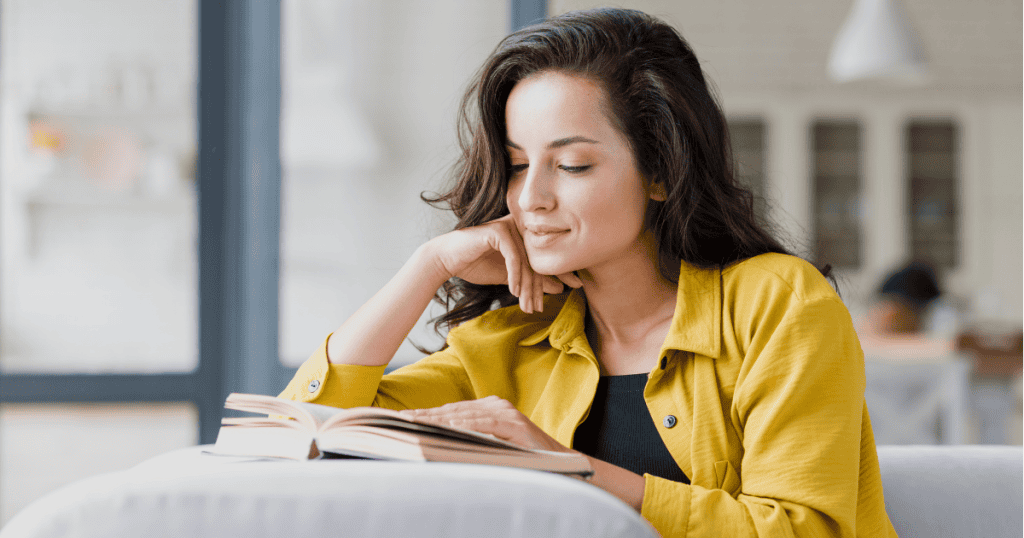 A woman rests her chin on her hand while quietly engrossed in reading an open book, reflecting the calm, educated perspective that renders manipulative tactics completely useless.