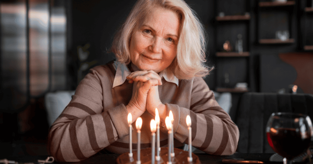 An older woman smiles knowingly with her hands clasped behind a lit birthday cake, reflecting how a narcissist treats an apology as a debt rather than a step toward healing.