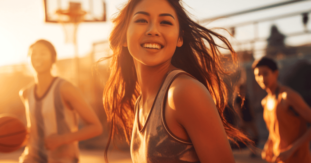 A young woman beams with joy while playing basketball with friends in the golden sunset light, showing the importance of holding onto what genuinely makes you happy despite a narcissist’s attempts to dim it.