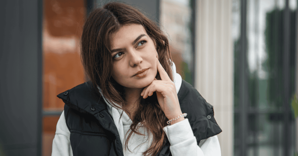 A young woman rests a finger on her chin with a thoughtful, discerning look, reflecting the growing ability to tell the difference between genuine kindness and a narcissist’s performance.