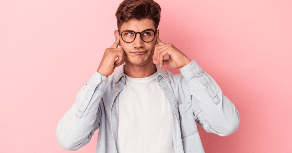 A young man plugs his ears and looks away with a dismissive expression, illustrating how a narcissist tunes out your pain while listening only for a mistake they can use against you.