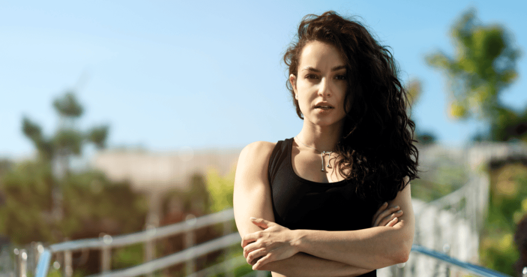A woman stands with arms crossed and a calm, steady gaze in the sunlight, reflecting the quiet strength of dealing with a narcissist without needing to confront them.