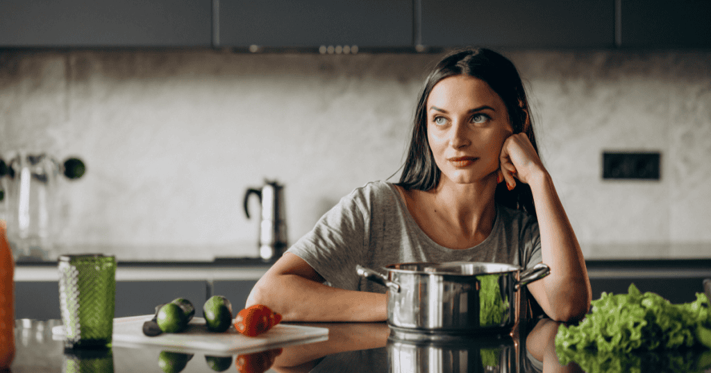 A woman leans on her kitchen counter with her chin in her hand and a thoughtful, composed expression, reflecting the quiet resolve of reclaiming your power from the unfinished business a narcissist left behind.