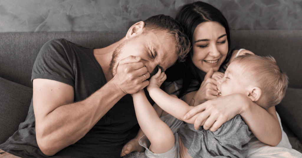 A laughing baby playfully grabs his father’s face as his mother smiles beside them, showing the kind of genuine, unstaged family joy that a narcissist’s polished image could never truly capture.