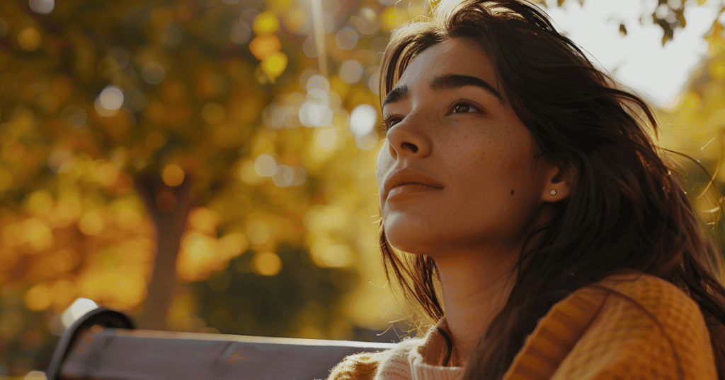 A woman sits on a park bench in warm autumn light, gazing upward with a calm, reflective expression, capturing the clarity of realizing a narcissist’s version of events was never the full story.