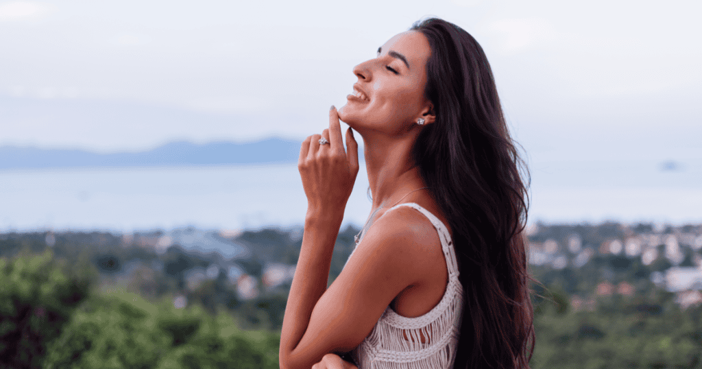 A woman tilts her face toward the sky with her eyes closed and a radiant smile, embracing the freedom of knowing a narcissist’s cruel words were never the truth about you.