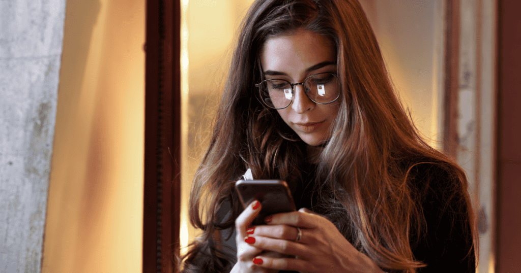 A woman in glasses calmly types on her phone with a focused, composed expression, showing the steady confidence of responding to a narcissist without falling back on an automatic apology.