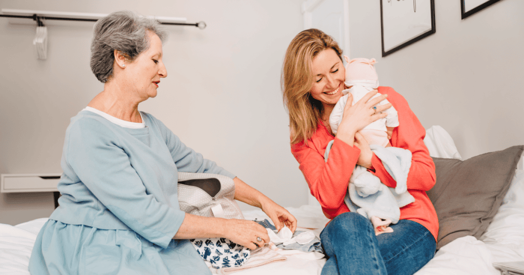 An older woman busies herself packing a baby bag while a young mother cuddles her newborn, hinting at the control and need for credit that can hide beneath a narcissist’s seemingly kind and helpful persona.