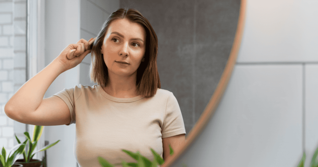 A woman brushes her hair in the mirror with an uncertain, self-conscious look, reflecting how a narcissist’s casual remarks about your appearance can leave you doubting yourself.