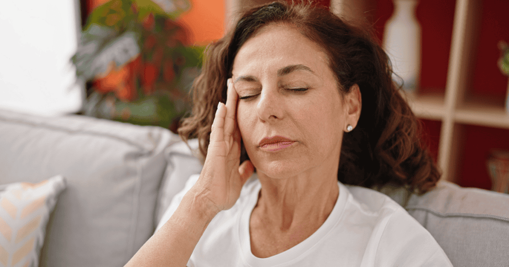 A woman closes her eyes and presses a hand to her temple in visible strain, capturing how a narcissist begins to fall apart once they can no longer control you.