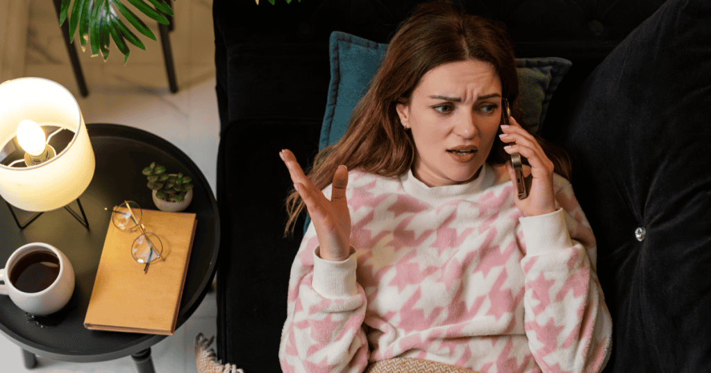 A frustrated woman on the phone throws up her hand in disbelief, capturing the confusion of apologizing to a narcissist even when you know you did nothing wrong.