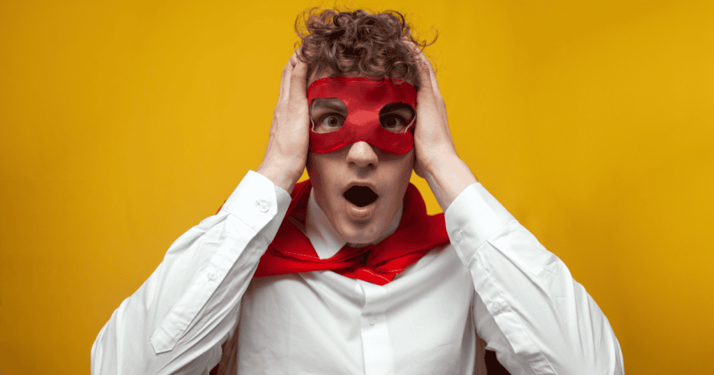 A young man in a red hero mask and cape clutches his head in shock, illustrating how a narcissist’s heroic act eventually cracks and can’t hold up over time.