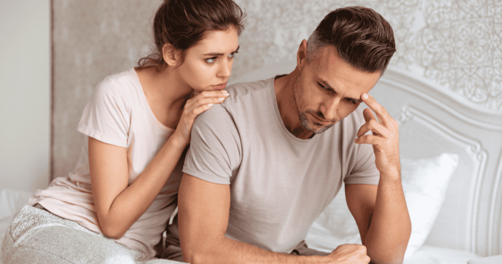 A worried woman leans on the shoulder of a withdrawn man who looks away with his hand to his head, showing how you can keep reaching for partners who are emotionally unable to love you back.