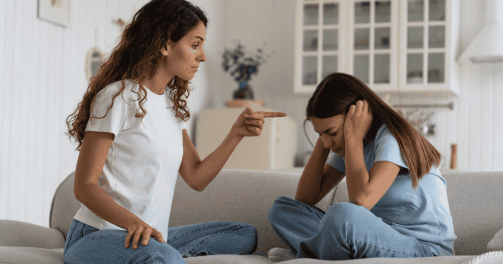 A woman points an accusing finger at a girl who covers her ears and looks down, illustrating how a narcissist revives old blame to see if they can still make you feel guilty.