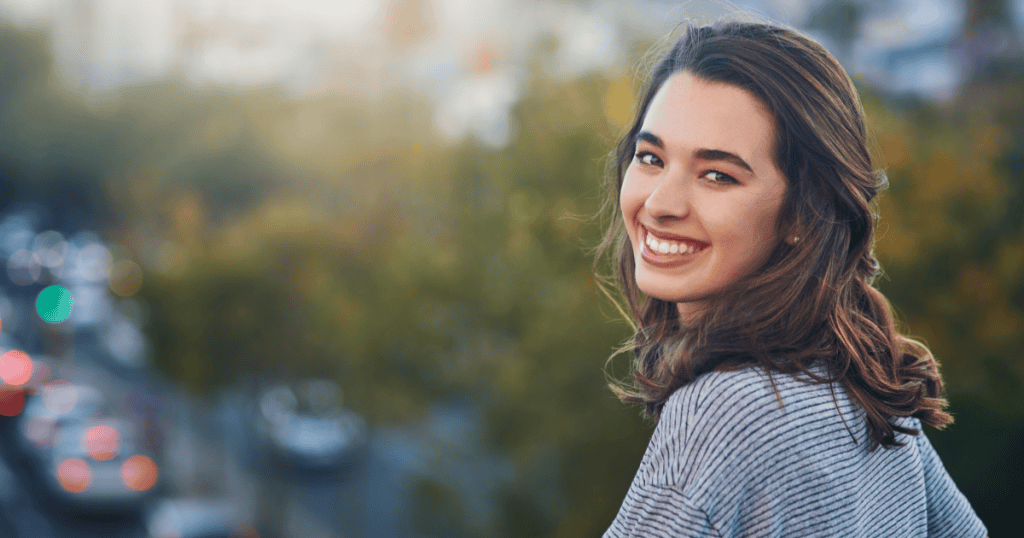 A young woman glances back over her shoulder with a bright, carefree smile, showing the freedom of refusing to play along with a narcissist’s tests and choosing yourself instead.