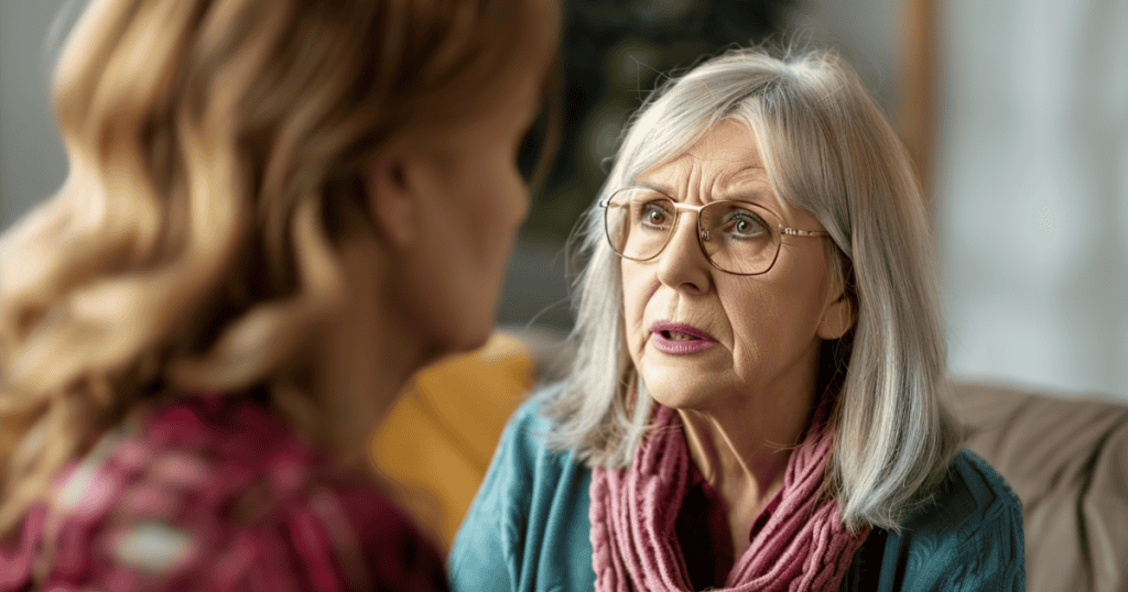 An older woman in glasses leans in and questions a younger woman with an intense, probing expression, illustrating how a narcissist uses interrogation-style questions to test whether they still have control over you.