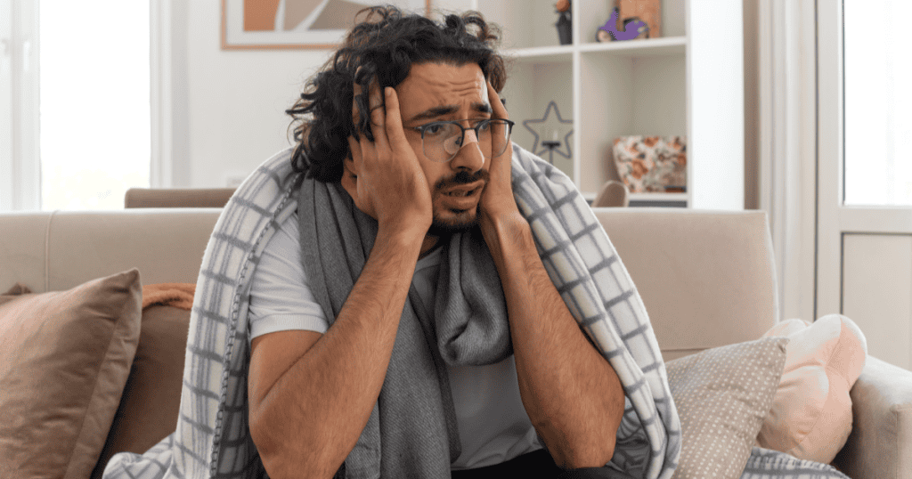 A man wrapped in a blanket clutches his face with an exaggerated look of distress, illustrating how a narcissist plays the misunderstood victim by telling others you just don’t understand them.