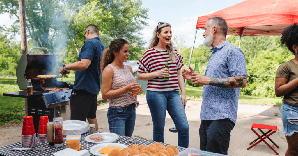 A woman laughs and chats easily with an older man and friends at a backyard barbecue, showing the warm welcome into someone’s circle that being kept at a distance by a narcissist was quietly denying you.