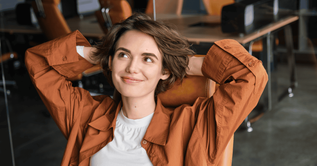 A woman leans back in her office chair with her hands behind her head and a content smile, showing the kind of self-made independence a narcissistic parent treats as betrayal.