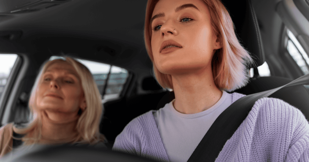A young woman with pink hair drives with a focused, self-assured expression while an older woman rests calmly in the passenger seat, reflecting the truth that you were never just another replaceable person in a narcissist's life.